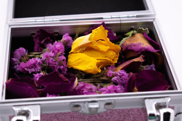 An open metallic box reveals a collection of vibrant, dried flower petals. The focal point is a...
