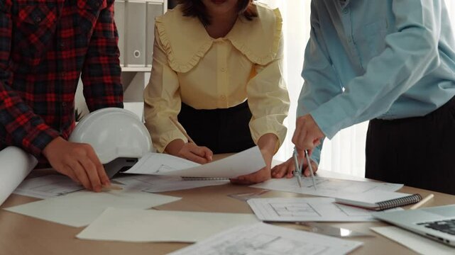 Architect and safety engineer discussion about building blueprint displaying on laptop on table with architectural document and wooden block scatter around at modern office. Closeup. Delineation.