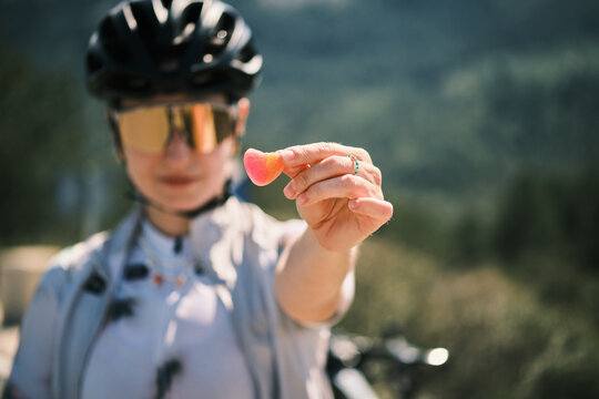Close-up of a cyclist holding a vibrant, heart-shaped gummy candy. The blurry background emphasizes the bright colors of the treat and the cyclist's gear. Calpe,Alicante. Spain