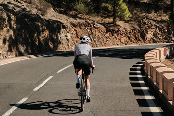 Female cyclist rides a road bike on a scenic mountain road.  Sunlight casts shadows. Active...