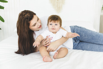 Mother and child love. Tender portrait of a young mother and her 7 month old baby sitting on a soft white bed in a bright sunny bedroom. 