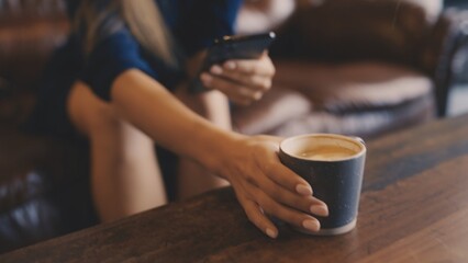 Close-up of woman scrolling on her phone while sipping coffee in a warm cafe atmosphere