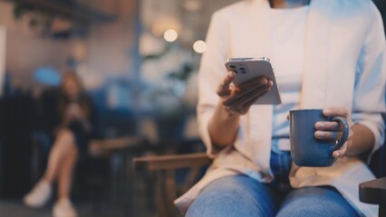 Closeup of coffee shop visitor on smartphone while sipping coffee, casual lifestyle