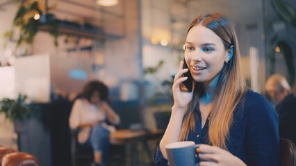 Young smiling woman talking on phone with friend in coffee shop, vibrant urban lifestyle
