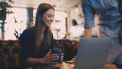 Young woman receiving bill from waitress in coffee shop, satisfied customer experience