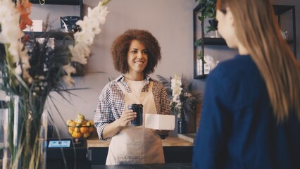 Smiling woman handing coffee and cake to-go to client in cafeteria, friendly service
