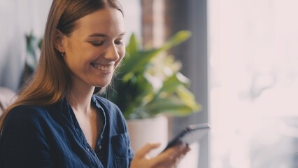 Cheerful young woman smiling while chatting on smartphone, reacting to positive news