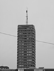 Black and white photo of a high-rise building in Warsaw with rooftop antenna, minimalist composition highlighting urban architecture against a blank sky.