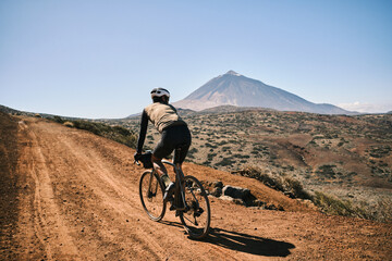 Cyclist on gravel road with majestic volcano in background. Epic adventure, stunning landscape,...