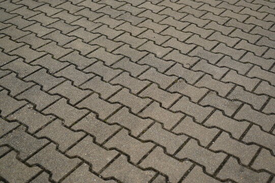 Concrete paving stone texture with interlocking zigzag pattern. Gray sidewalk surface background for architecture, urban design, and construction projects. Outdoor pavement made of shaped concrete blo