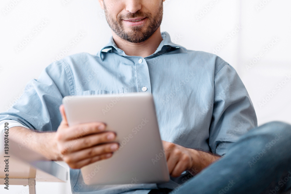 Poster portrait of handsome young man using digital tablet during break in office, browsing internet or soc