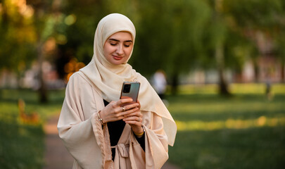 A young happy Muslim woman in hijab using a phone outside