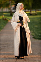 Full length portrait of a beautiful Muslim woman wearing elegant modern fashion hijab outside.