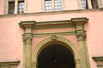 Obraz premium historic European building facade with decorative architectural details and an ornate inscription below the windows. Classical style exterior with stone framing and pastel walls.