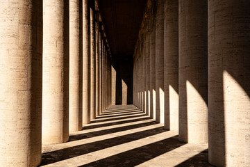 Symmetrical stone colonnade with strong shadows and warm light. Architectural rhythm and dramatic perspective create a powerful abstract urban composition