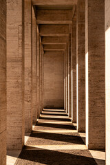 Symmetrical stone corridor with tall columns and dramatic shadows. Abstract urban architecture with...