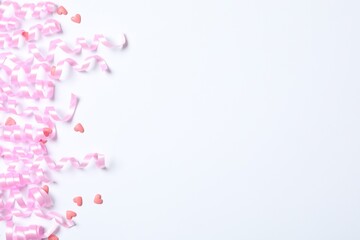 Pink serpentine streamers and heart shaped confetti on white background, top view