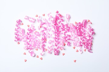 Pink serpentine streamers and heart shaped confetti on white background, top view
