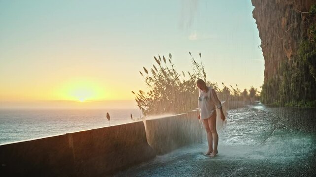 Young woman enjoying her vacation under waterfall in Madeira at sunset, with ocean in background