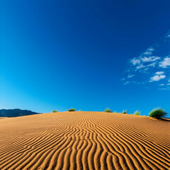 Naklejka premium Textured Sand Dunes Under a Bright Blue Sky with Distant Hills and Small Plants