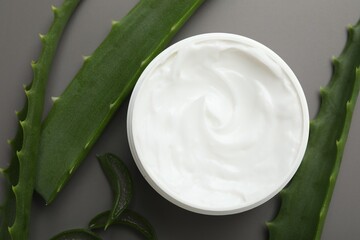 Moisturizing cream with extract of aloe vera in jar and cut leaves on grey background, flat lay