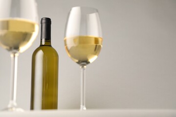 Tasty white wine in glasses and bottle on light grey background, low angle view. Space for text