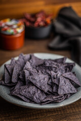 Dark nachos chips on plate on wooden table.
