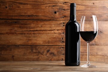 Tasty red wine in glass and bottle on wooden table, space for text