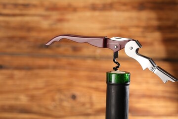 Bottle of luxury wine with corkscrew on blurred background, closeup. Space for text