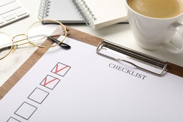 Checklist with marked checkboxes, stationery, glasses and coffee on white table, closeup