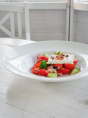 Salad with tomatoes and feta cheese. Vegetable salad on white plate on white table in white gazebo.