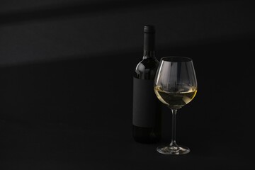 Bottle of wine and wineglass on black background, space for text