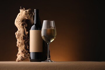 Bottle of wine, tree bark and wineglass on brown table against dark background, space for text