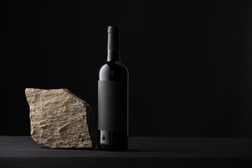 Bottle of wine and rock on black table, space for text