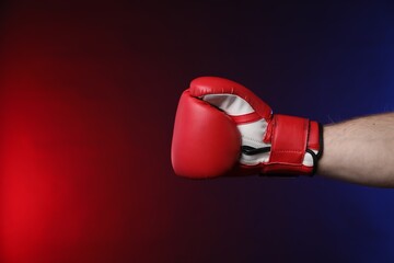 Man with boxing glove fighting on dark background in neon lights, closeup. Space for text