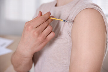 Man making insulin injection into his arm indoors, closeup. Diabetes