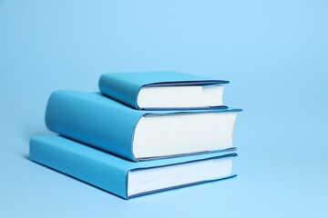 Stack of different books on light blue background, closeup. Space for text