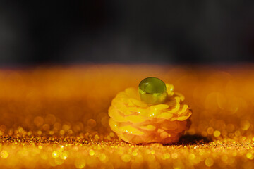 A dreamy macro shot of a yellow buttercup with a green water droplet, set against a glowing golden...