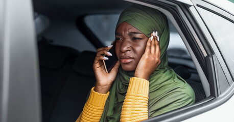 Black Muslim Lady In Hijab Suffering Bad Connection While Talking On Cellphone In Car, Sitting On Back Seat And Covering Ears, Displeased Islamic Woman Trying To Hear Conversation, Free Space