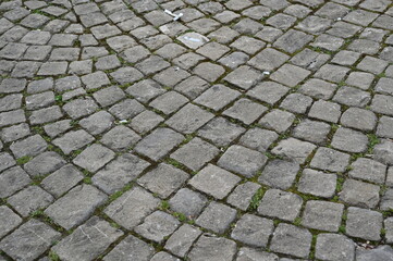 Old cobblestone pavement with irregular stone pattern. Historic European street texture with weathered stones and moss between the gaps