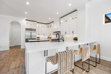 A kitchen with white cabinets, a large island, stools, and fridge