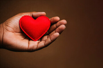 Fototapeta premium Red heart in palm on brown background. Space for text.