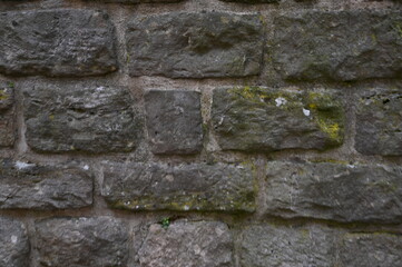Gray stone wall with moss texture, old masonry background. Natural rough surface, historical architecture detail, and aged stone pattern.