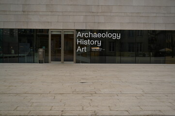 Modern museum or academic building facade with large glass windows and the text “Archaeology – History – Art” displayed on the entrance. Minimalist stone architecture suitable for culture, education, 