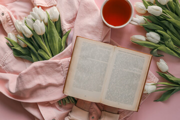 Flat lay of a cozy spring scene with a pink denim jacket, an open vintage book, a bouquet of white...
