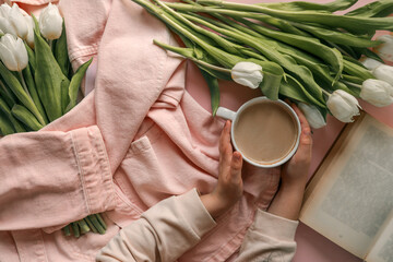 Cozy flat lay with a pink denim jacket, white tulips, an open book, and a cup of coffee held by a...