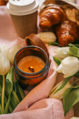Cozy still life with a burnt candle in an amber glass jar surrounded by white tulips, a pink denim...