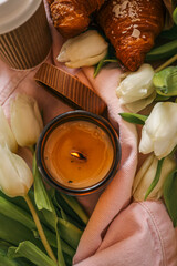 Cozy still life with a burnt candle in an amber glass jar surrounded by white tulips, a pink denim...