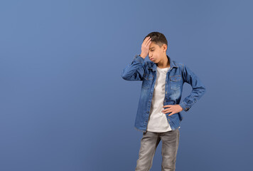 Portrait of exhausted young businessman with head in hand standing frustratingly against blue background
