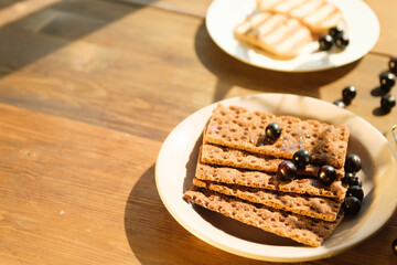 A plate holds crunchy snacks topped with fresh blackberries, placed on a rustic wooden table bathed...